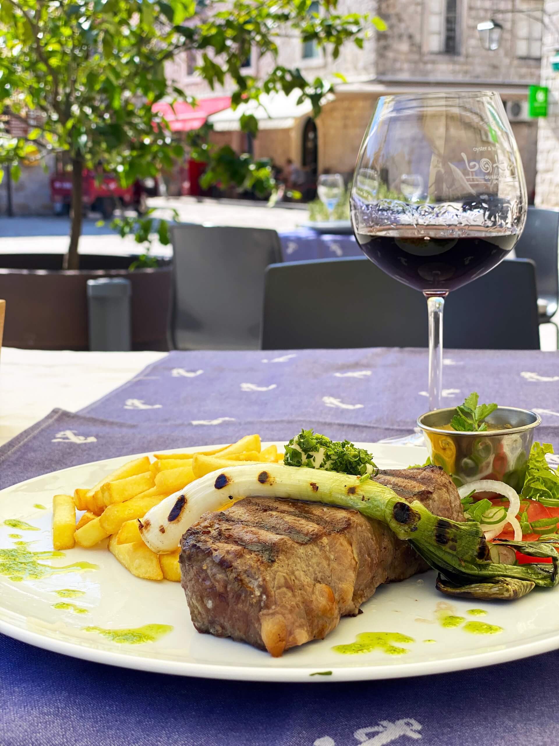 Un filetto di manzo alla griglia con patatine fritte e un bicchiere di vino rosso del Pelješac.